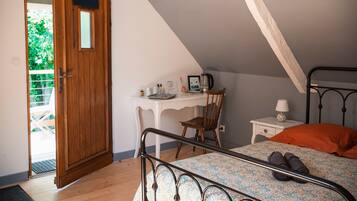 Une chambre avec un plafond en pente, une porte en bois, un bureau avec une chaise, un lit avec un cadre en métal et une table de chevet avec une lampe.