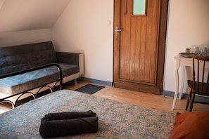 Una habitació petita i acollidora amb un sofà, una porta de fusta, una taula petita amb una tassa i una cadira.
