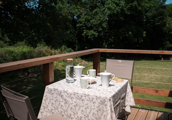 An outdoor table set with a teapot, cups, and a bottle, surrounded by a wooden deck and a grassy area. - Guest Room 'La Corzic' (Pléguien)