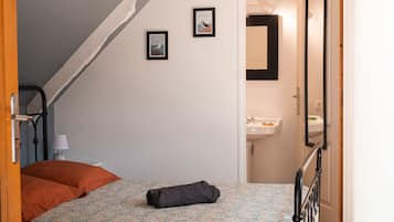 Ett sovrum med en säng, en hoprullad handduk, ett nattduksbord med en lampa och en tavla som hänger på väggen.