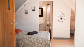 Une chambre à coucher avec un lit, une petite fenêtre et une porte donnant sur une salle de bain.