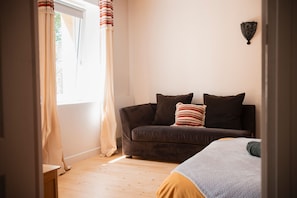 Habitació amb un sofà, dos coixins, una làmpada de paret i una finestra amb cortines.