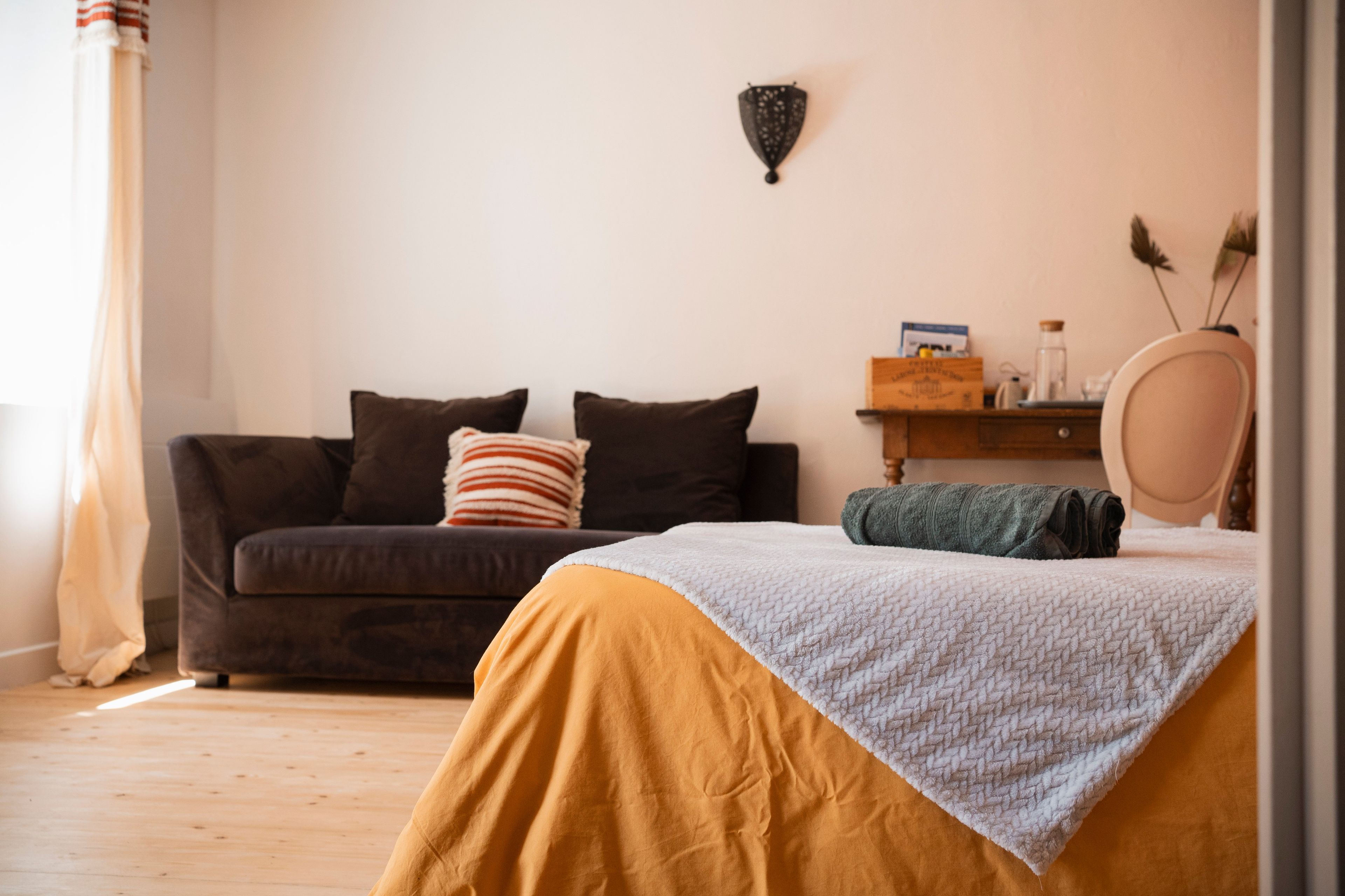 Een slaapkamer met een bed, een slaapbank, een nachtkastje en een wandlamp.