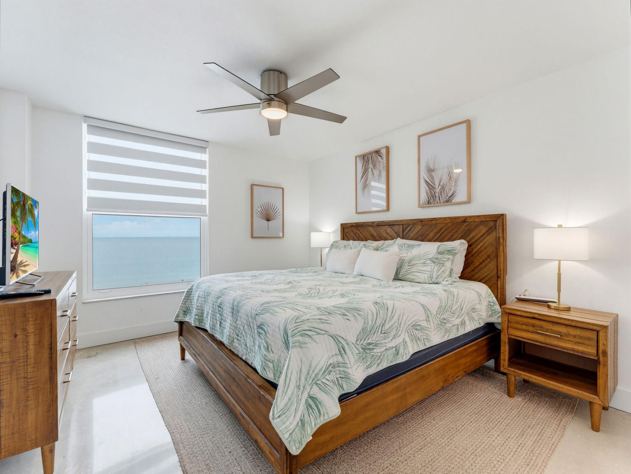 A bedroom with a bed, bedside tables, a ceiling fan, a window with blinds, and wall art.