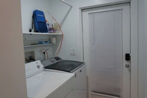 Un'area lavanderia con lavatrice, asciugatrice e una borsa blu su uno scaffale.
