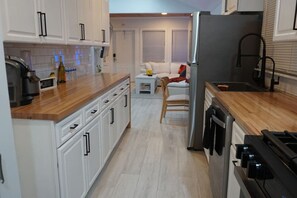 Una cucina compatta con mobili bianchi, un piano di lavoro in legno, un frigorifero e un fornello.