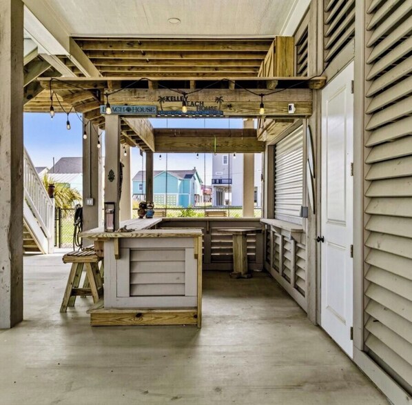 Ein überdachter Außenbereich mit Holzkonstruktion, einem Schild mit der Aufschrift 'Kelley Beach House' und Blick auf die Nachbarschaft.
