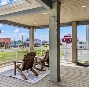 Ein überdachter Außenbereich mit Holzstühlen und Blick auf den Strand und die Gebäude.