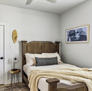 Ein Schlafzimmer mit einem hölzernen Bett, einer weißen Wand, einem gerahmten Bild und einem kleinen Nachttisch.