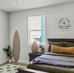 Ein Schlafzimmer mit einem Bett, einem Surfbrett, einem Fenster mit Jalousien und einem Wandzeichen.