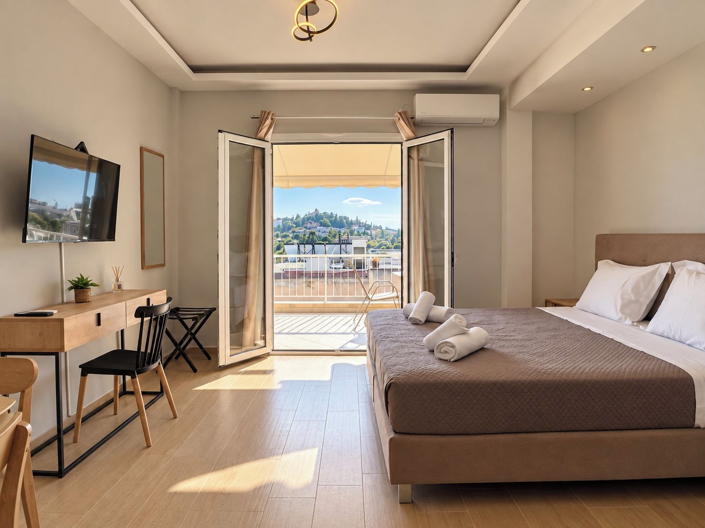 A hotel room with a bed, a desk, a chair, a television, and a balcony with a view.
