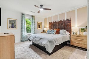 A bedroom with a bed, a nightstand, a dresser, a ceiling fan, and a window with curtains. - Brand-New 4BR/3BA Home on Dayton’s West Side (Trotwood)