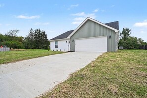 A single-story building with a garage, a driveway, and a grassy yard. - Brand-New 4BR/3BA Home on Dayton’s West Side (Trotwood)