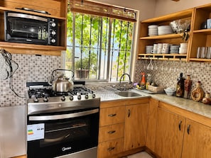 A kitchen with a stove, oven, microwave, and a window with a view of greenery. - Cabaña del Bosque - Laguna Verde (Valparaiso)