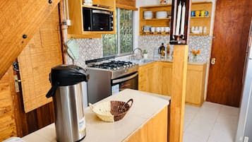 Una cocina pequeña con armarios de madera, microondas, estufa y hervidor.