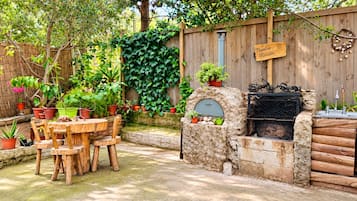 A patio with a stone oven, wooden table, and chairs, surrounded by potted plants and a wooden fence.