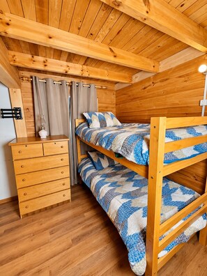 A bunk bed with a patterned bedspread, a wooden dresser with drawers, and a lamp on a wooden floor. - Cabaña del Bosque - Laguna Verde (Valparaiso)