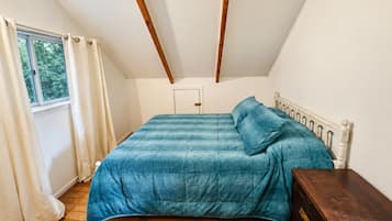 Un dormitorio con cama, piso de madera, ventana con cortinas y una puerta.