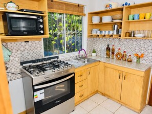 A kitchen with a gas stove, oven, microwave, and a window with a view of greenery. - Cabaña del Bosque - Laguna Verde (Valparaiso)