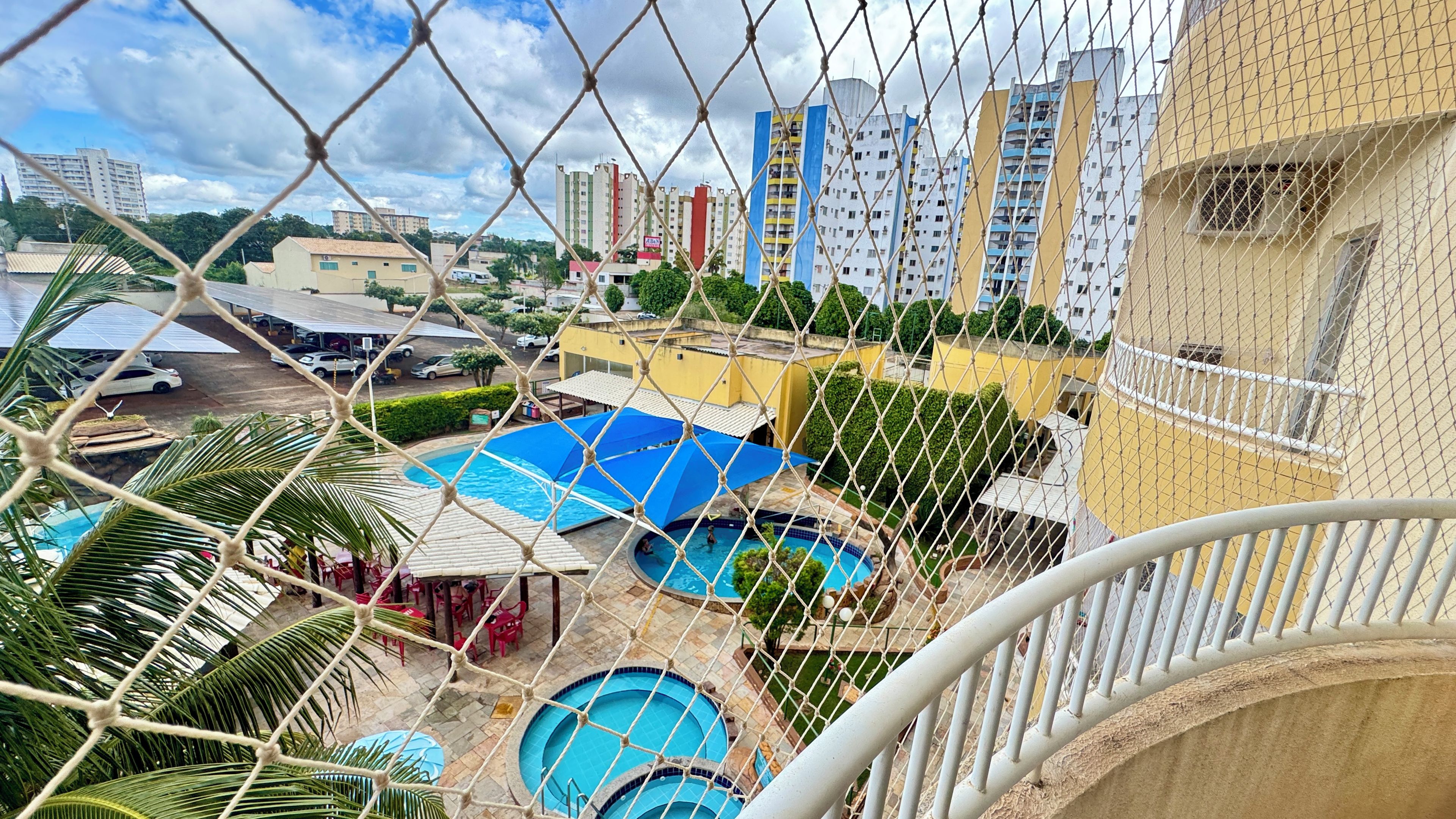 Área residencial com várias piscinas, um parquinho cercado e edifícios altos ao fundo.