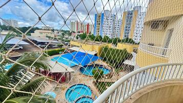 Área residencial com várias piscinas, um parquinho cercado e edifícios altos ao fundo.
