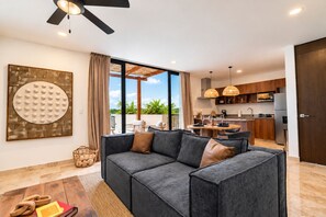 A modern living room with a grey sectional sofa, a dining area with a round table, and a kitchen with wooden cabinets and pendant lighting. - Gran Haven | Prv Hot Tub + Pool | 5 Min to Beach (Tulum)
