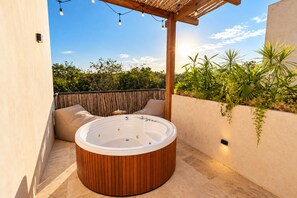 Ein Whirlpool mit Holzverkleidung, eine Pergola mit Lichterketten und Blick ins Grüne.