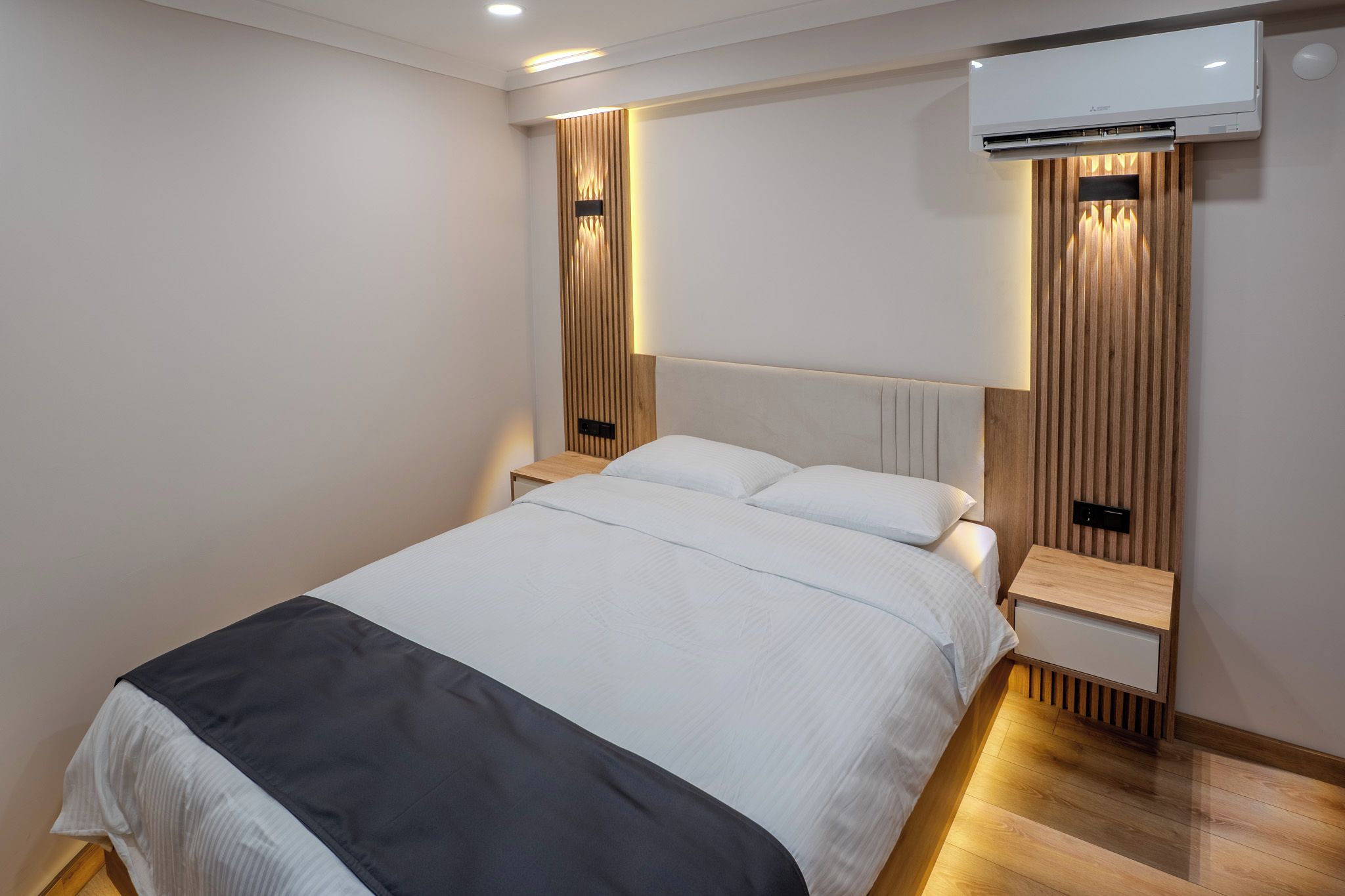 Una habitación de hotel moderna con una cama grande, cabecero de madera e iluminación integrada.