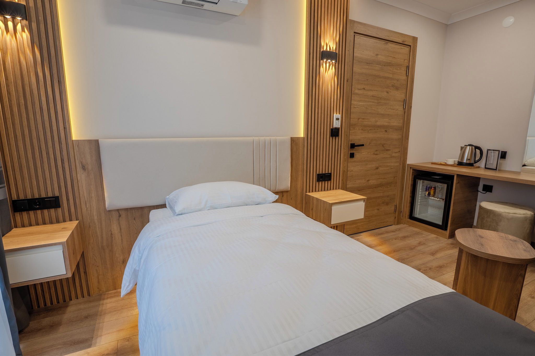 Una camera d'albergo moderna con un letto, comodini, un minibar e un armadio in legno.