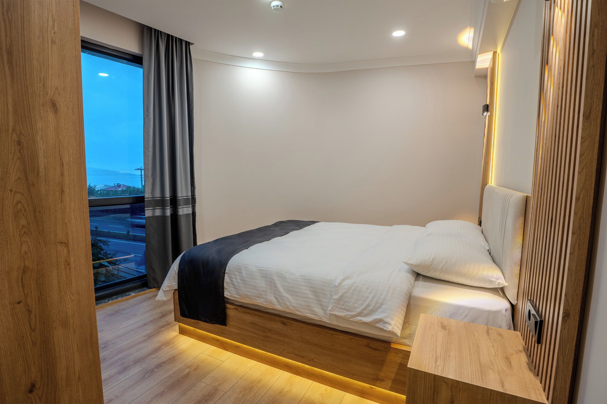 Une chambre d’hôtel moderne avec un lit, une vue sur l’extérieur et une tête de lit en bois.