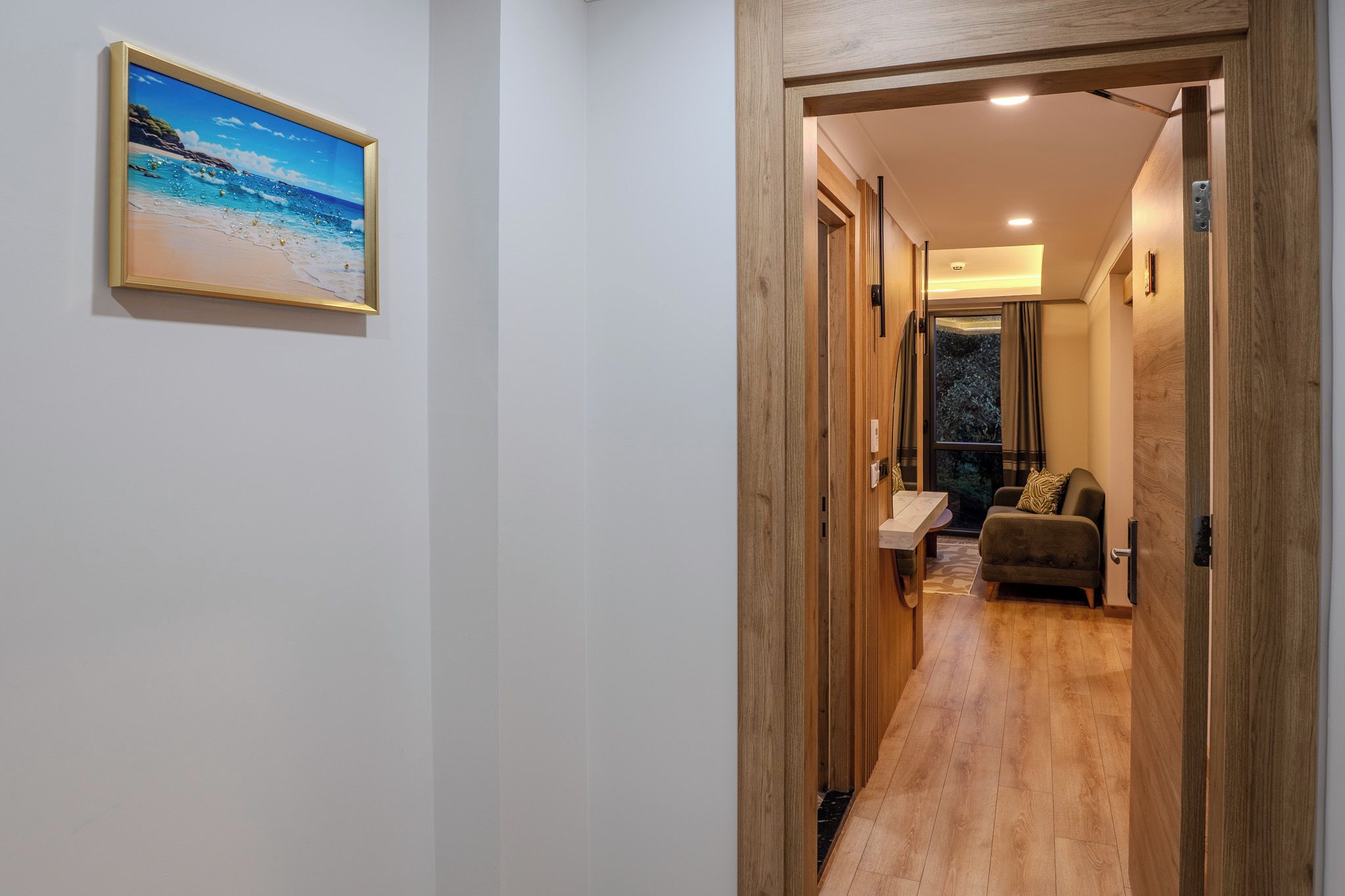 A hallway with wooden flooring, a framed picture on the wall, and a seating area with a couch and a small table.