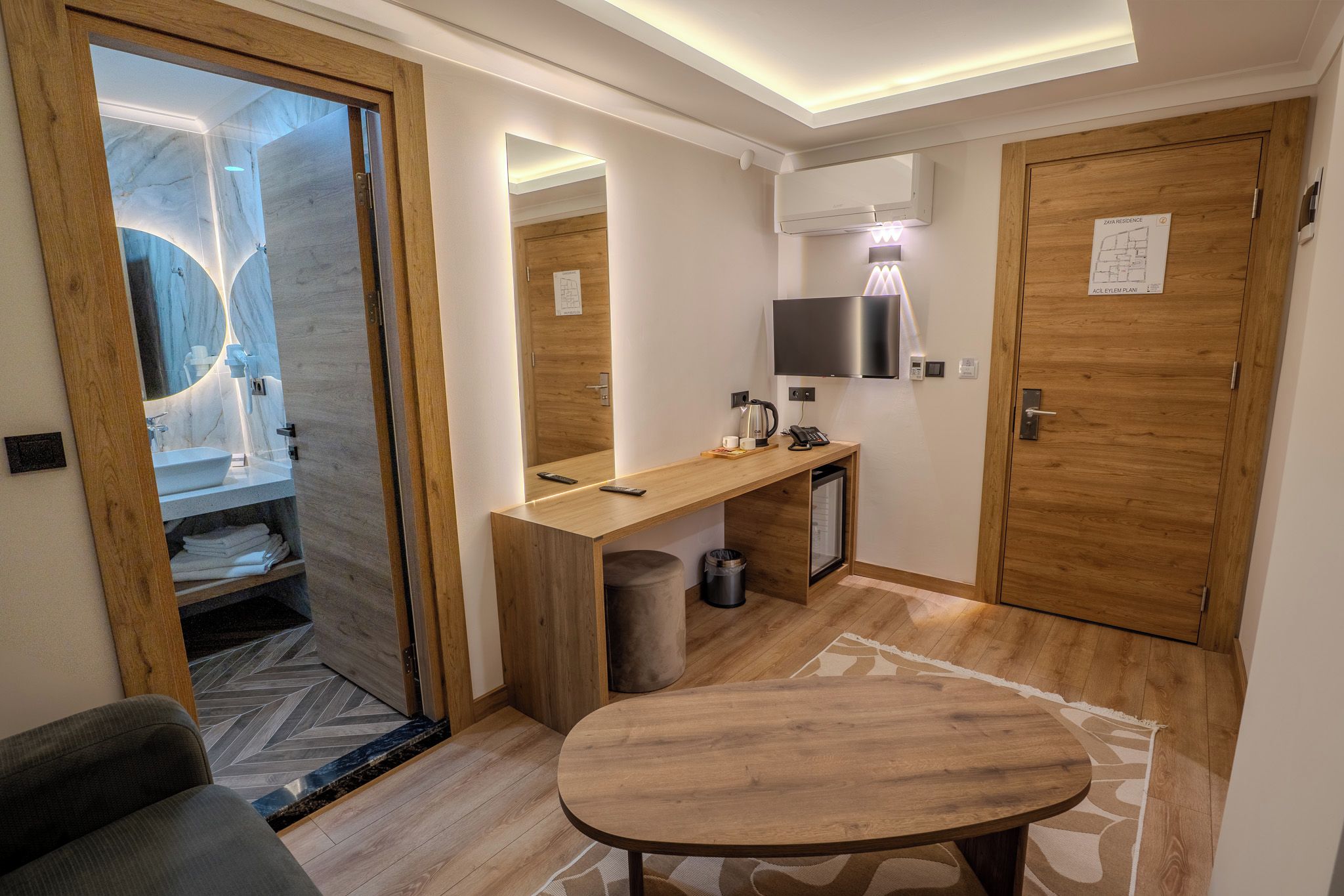 Un bagno moderno con un mobile lavabo in legno, uno specchio, un lavandino e un water. Si nota anche un piccolo tavolo e un cestino.