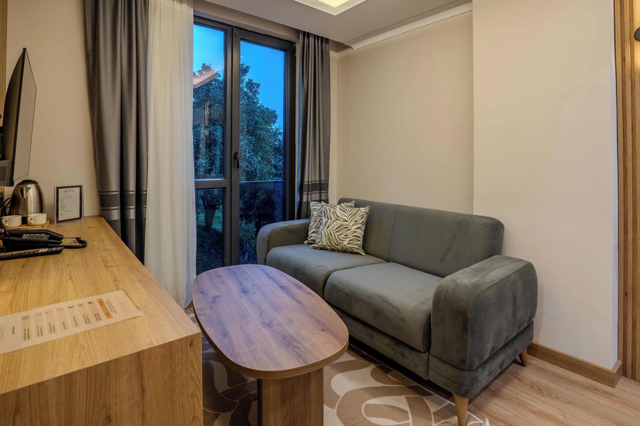 A modern room with a wooden desk, a grey sofa, and a window with curtains.