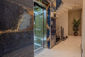 Un interior modern amb una escala de marbre, un ascensor de vidre i una planta en test.