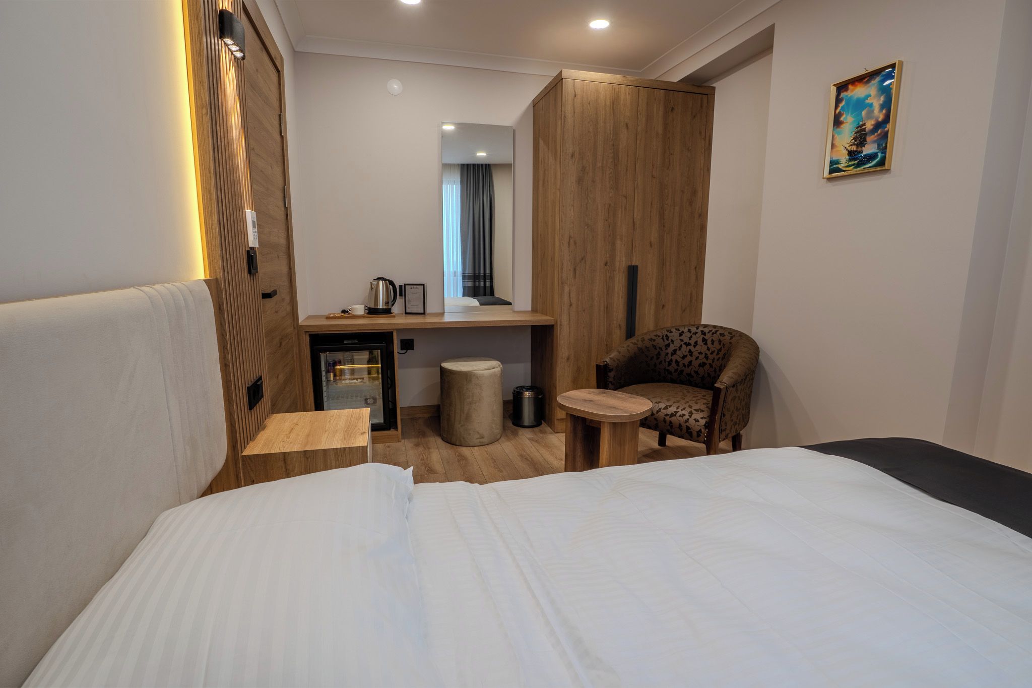 Een hotelkamer met een bed, een klein bureau, een stoel, een spiegel en een schilderij aan de muur.