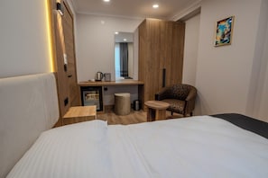A hotel room with a bed, a small desk, a chair, a mirror, and a painting on the wall. - Zaya Residence (Yomra)