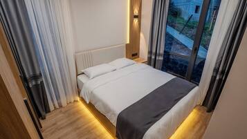 Een moderne slaapkamer met een groot bed, houten hoofdbord en uitzicht door een raam.