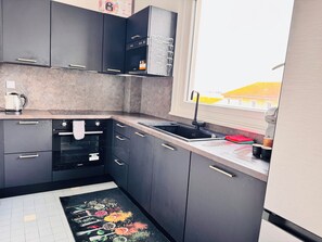 A modern kitchen with dark cabinets, a built-in oven, a stainless steel sink, and a window providing a view of the outside. - Right in the heart of Valence! 3-bedroom apartment, ideal for families and business trips (Valence)