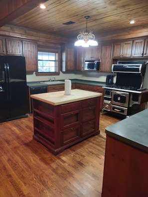 A kitchen with wooden cabinets, a central island with drawers, a refrigerator, a microwave, and a stove. - Spacious 4-bedroom house in charming Athens with AC (Athens)