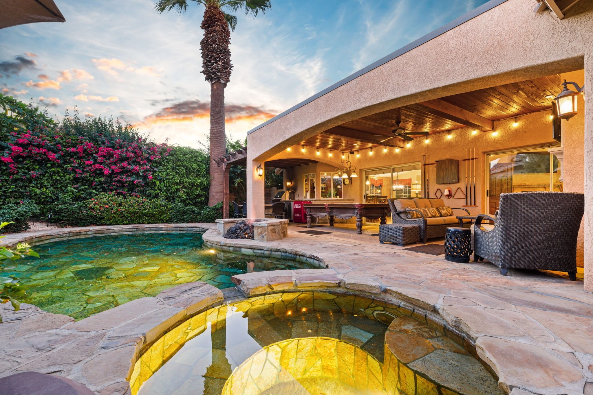 A pool area with stone steps, outdoor furniture, and a covered patio with string lights.