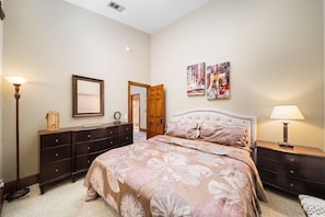 A bedroom with a large bed, a dresser, a nightstand, a floor lamp, and a mirror. - Pool, Spa & Game Patio Oasis in Indian Wells (Indian Wells)