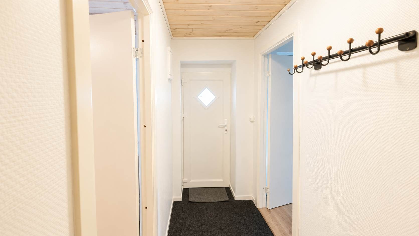 A narrow hallway with a door at the end, a coat rack on the right, and a mat at the entrance.