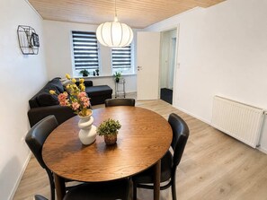 A modern living room with a round wooden dining table, black leather chairs, a white vase with flowers, and a pendant light. - Klaksvik Mountain View Stay (Klaksvík)