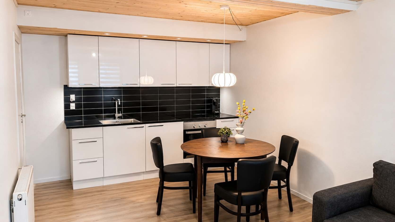 A modern kitchen with white cabinets, a black backsplash, and a round wooden dining table with chairs.