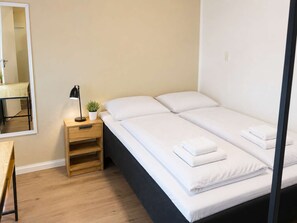 A single bed with white bedding and two pillows, a bedside table with a lamp, and a small potted plant. - Klaksvik Mountain View Stay (Klaksvík)
