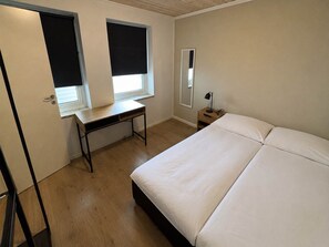 Un dormitorio con cama, escritorio y mesita de noche.