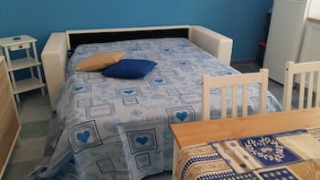 Une petite chambre avec un lit simple, une couvre-lit à motifs, un oreiller bleu et une chaise en bois.