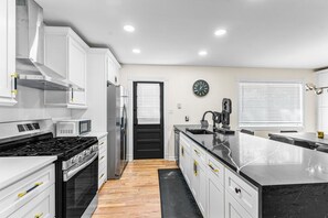 A modern kitchen with white cabinetry, a black countertop, and a stainless steel refrigerator. - Group Getaway- Theater Room + Game Room (Forest Park)