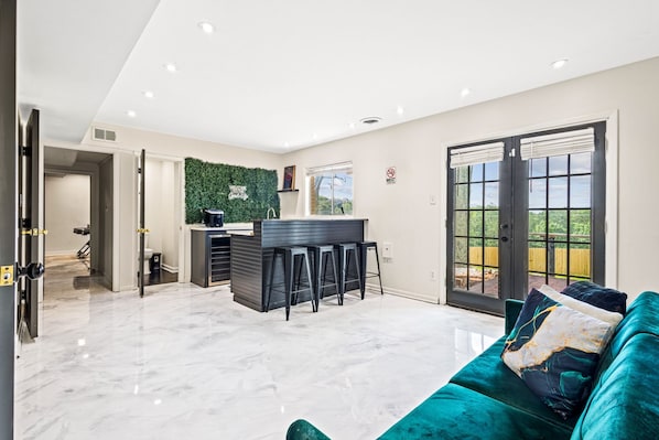 A spacious living area with a modern kitchen, a green wall, and a sliding glass door leading to a balcony. - Group Getaway- Theater Room + Game Room (Forest Park)