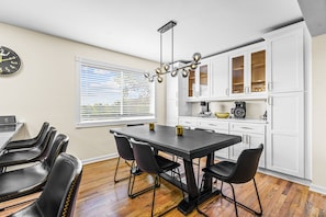 A modern kitchen with white cabinets, a black dining table, and a chandelier. - Group Getaway- Theater Room + Game Room (Forest Park)